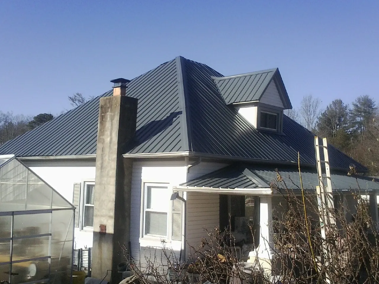 Dark blue standing seam metal roof on a white farmhouse with dormer — Slate & Tile Roof Repair by Roofing Brothers in Alex