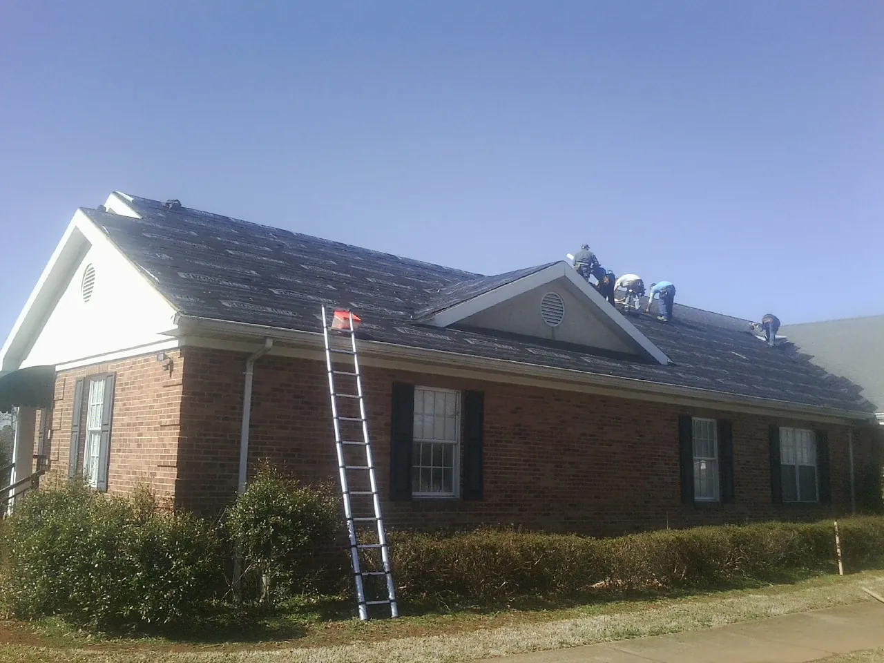 Crew tearing shingles off a brick ranch roof with a ladder set — Emergency Roof Repair work by our crew in Alex