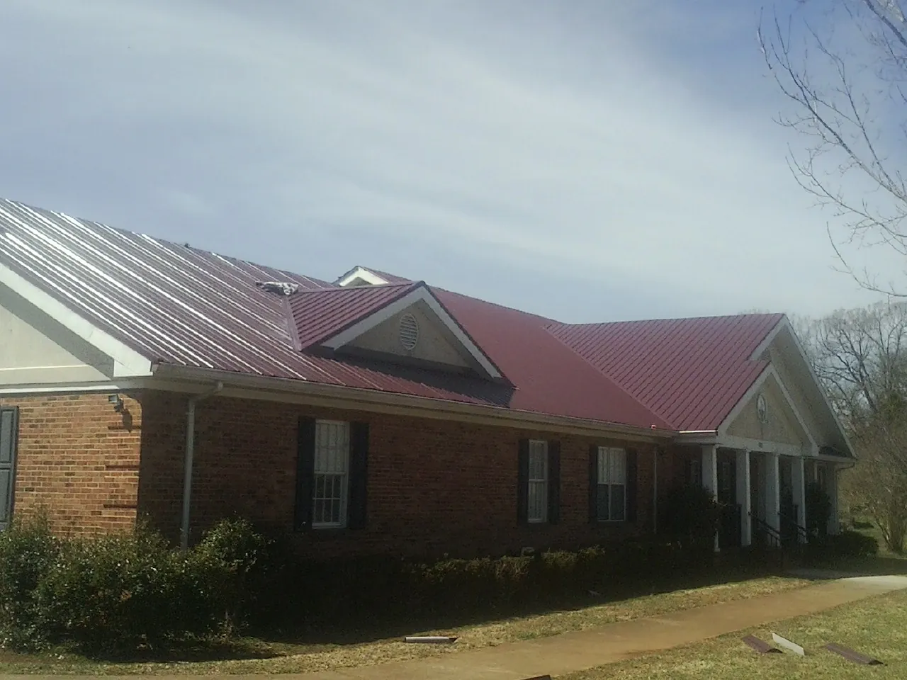 Red metal roof with gabled entries on a long brick building, from a Hail Damage Roof Repair job in Alex