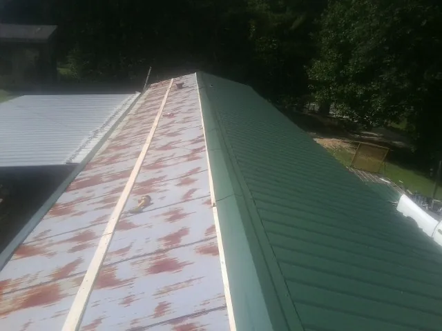 Old rusted panels beside newly installed green metal roofing — Wind Damage Roof Repair by Roofing Brothers in Alex
