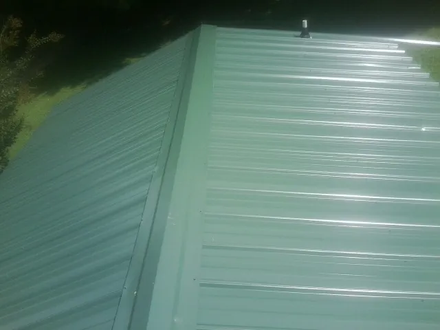New green metal panels meeting at the ridge of a roof — Flat Roof Repair work by our crew in Alex