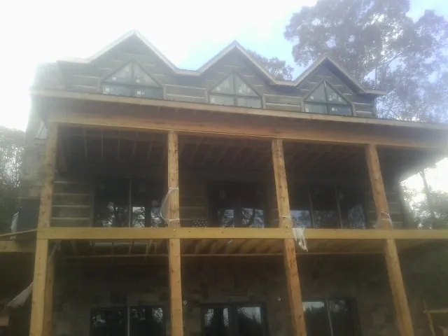 Dormers and porch framing on a large log home under construction — Roof Coating work by our crew in Alex