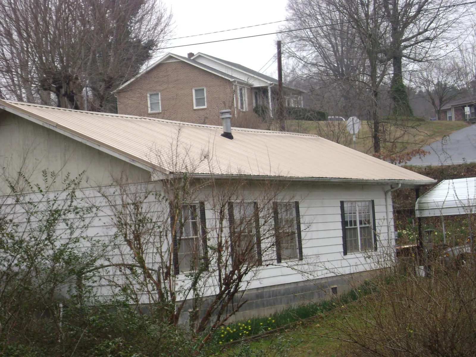 Tan metal roof on a white sided house set into a hillside — Commercial Roofing by Roofing Brothers in Alex