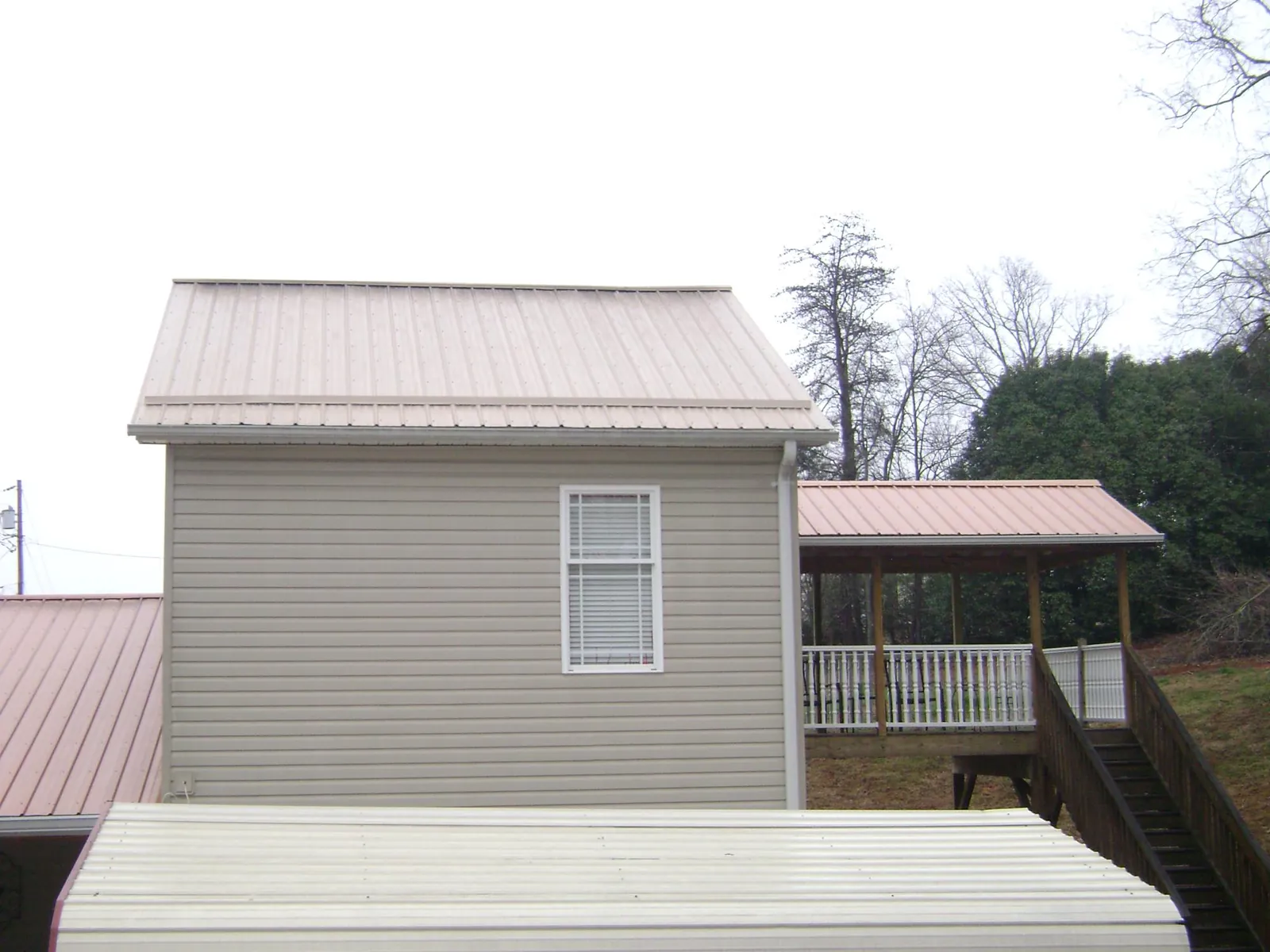 Tan metal roofs on a two story addition and attached porch, from a Roof Replacement job in Alex